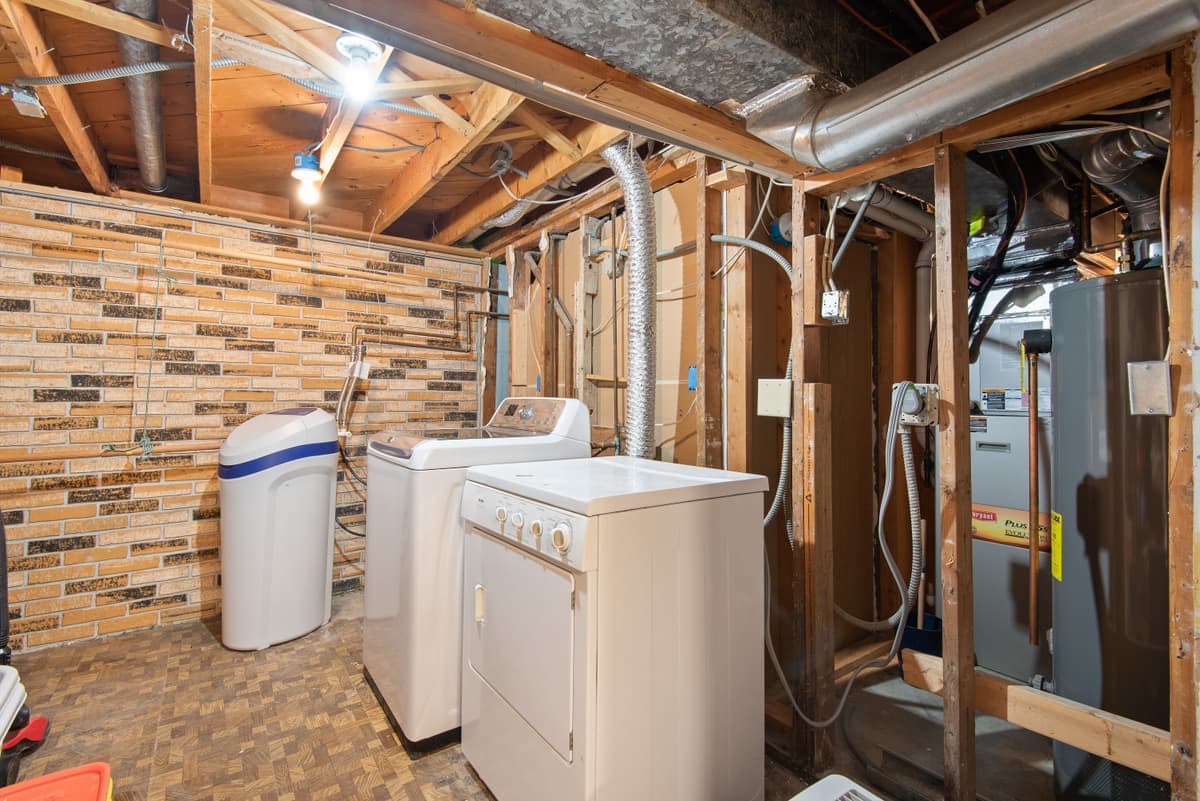 A washer and dryer in a plain utility space with pipework above