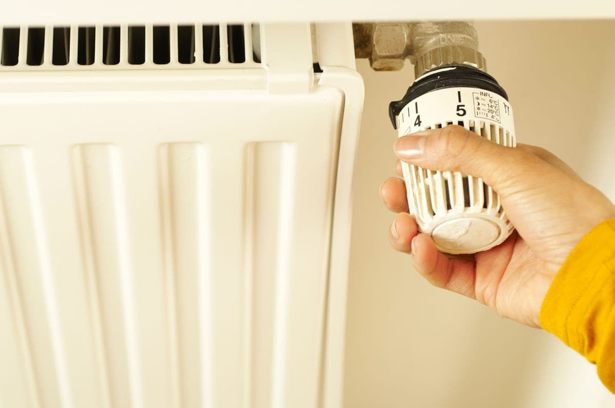 A hand turning a temperature dial on a heating valve
